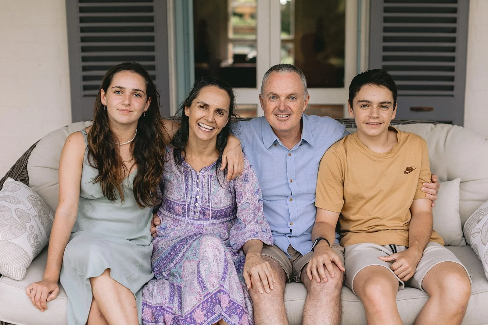 Mum, dad and their two teenagers smiling together on a verandah couch