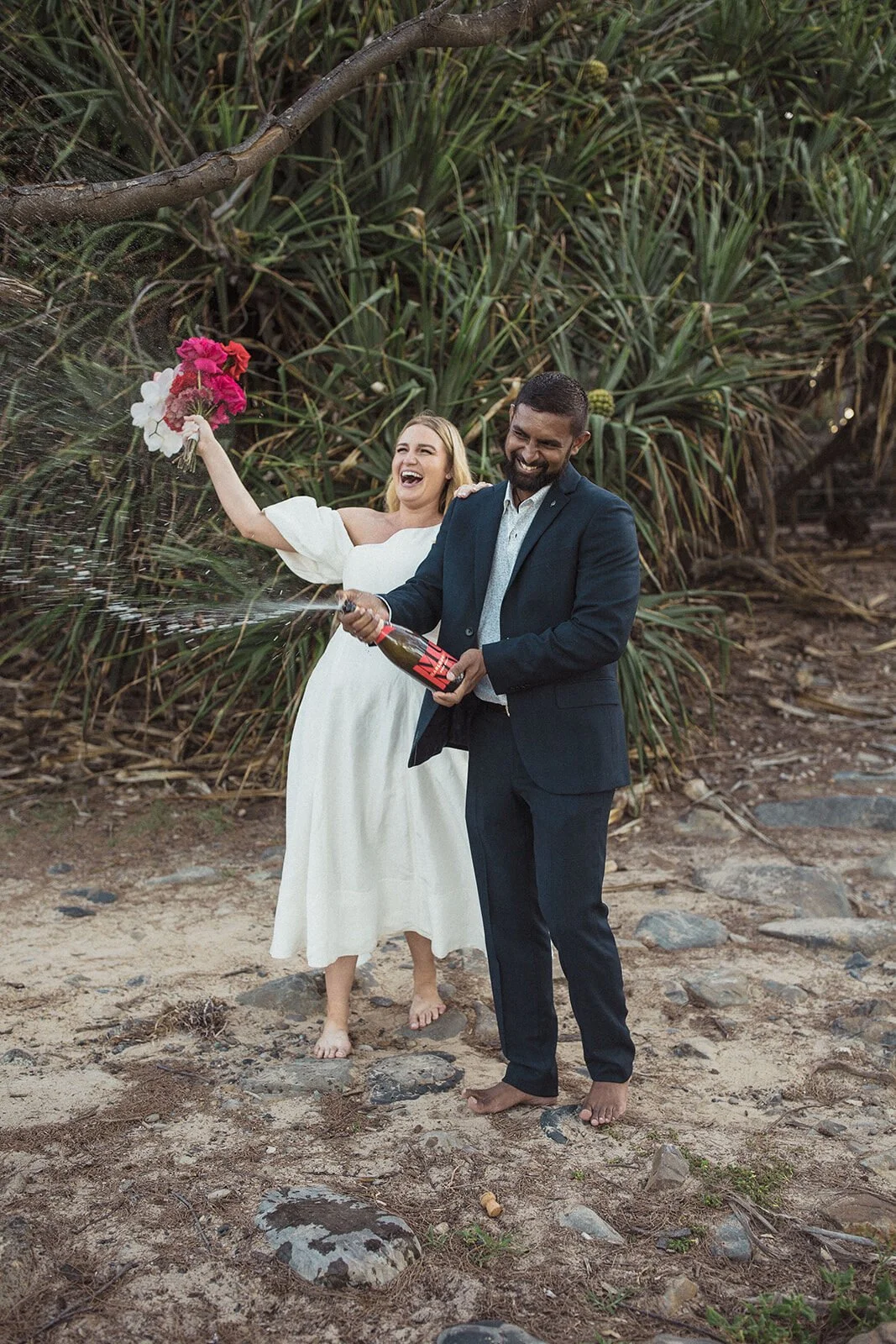 Couple popping champagne under pandanus trees, Brittany and Mark's elopement at Cabarita Beach, Northern Rivers