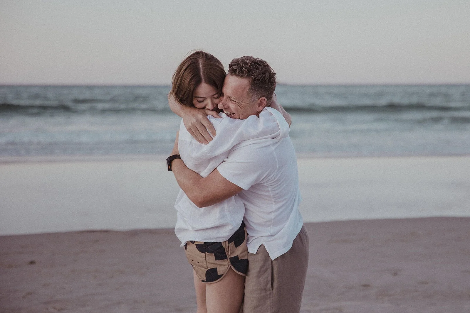 Couple hugging tightly at the shoreline after the proposal, Jamie and Jessica's beach marriage proposal at Belongil Beach, Byron Bay