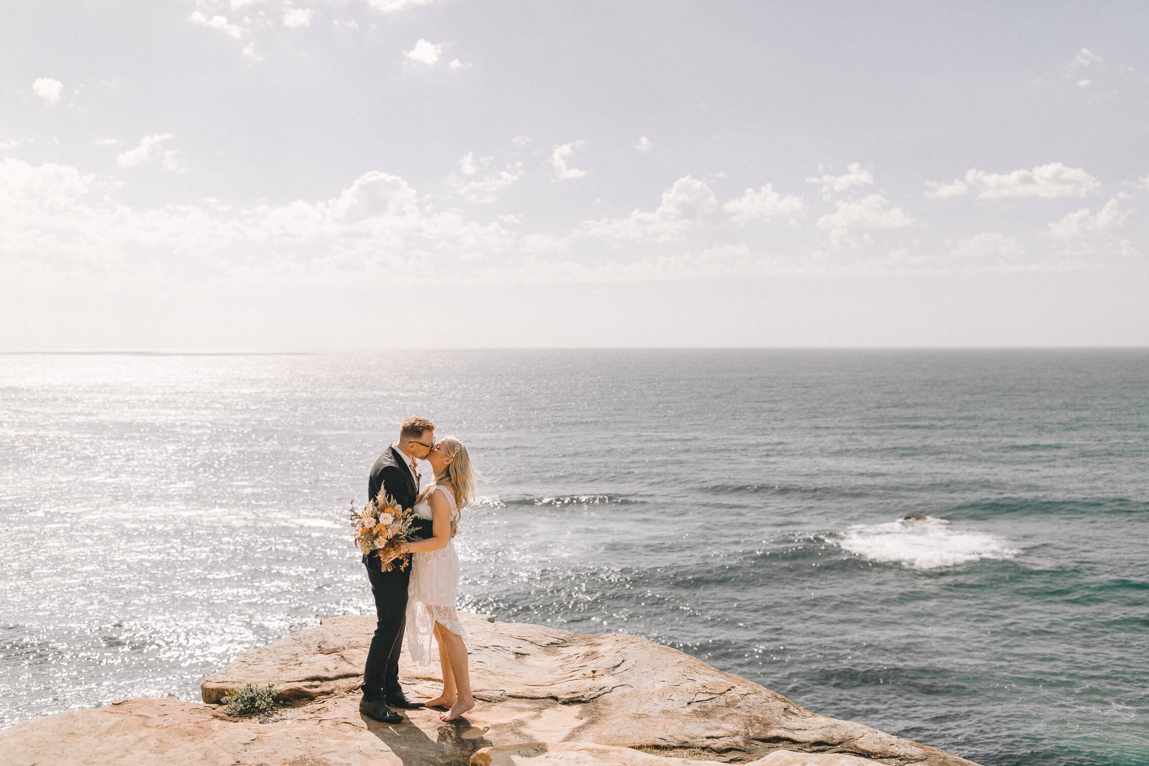 Bride and groom kissing on a clifftop above the ocean at Coogee