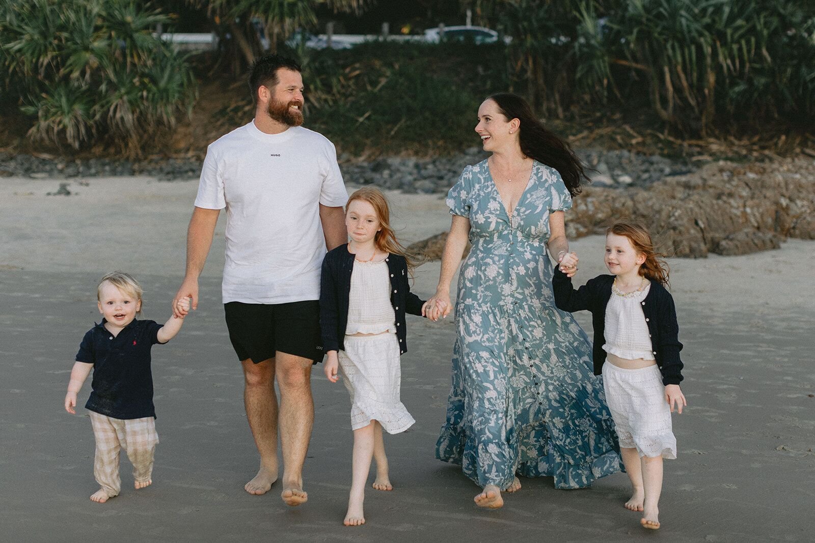 Family walking along the sand holding hands and laughing at Wategos Beach, Byron Bay