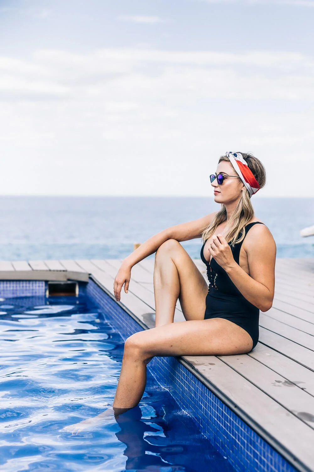 Woman in sunglasses and a headscarf relaxing beside an ocean pool