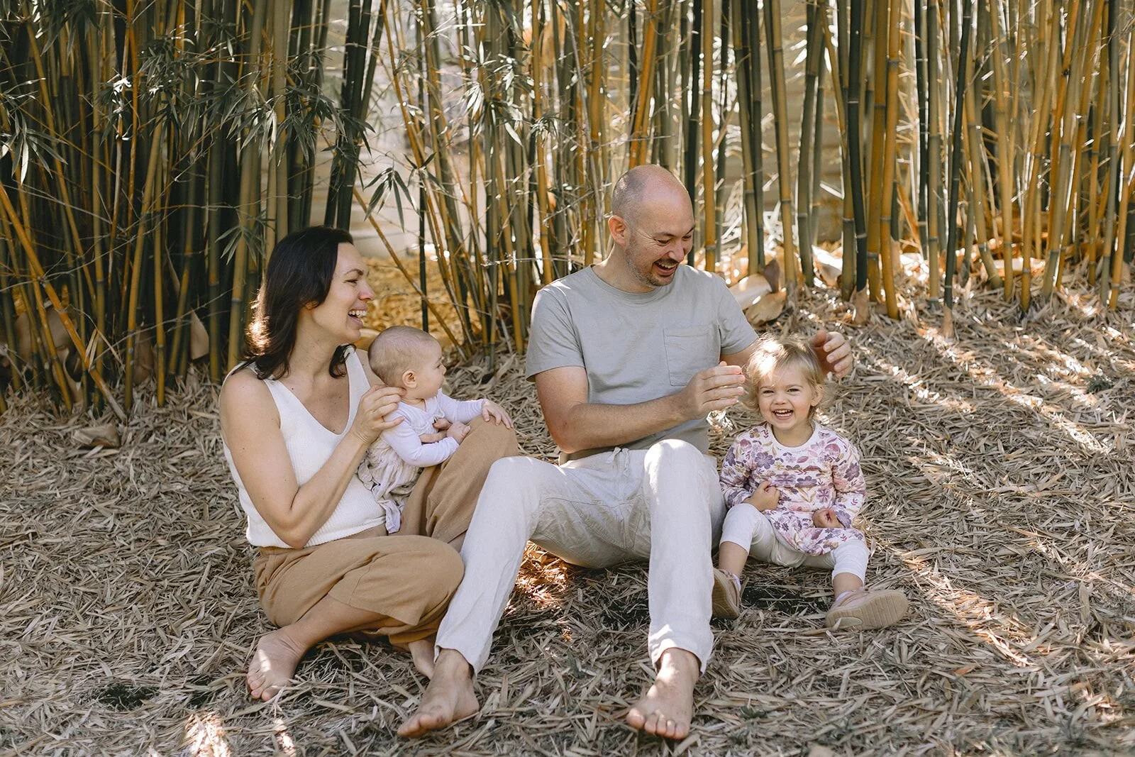 Family of four sitting on the bamboo leaf floor, mum and dad playing with their daughters