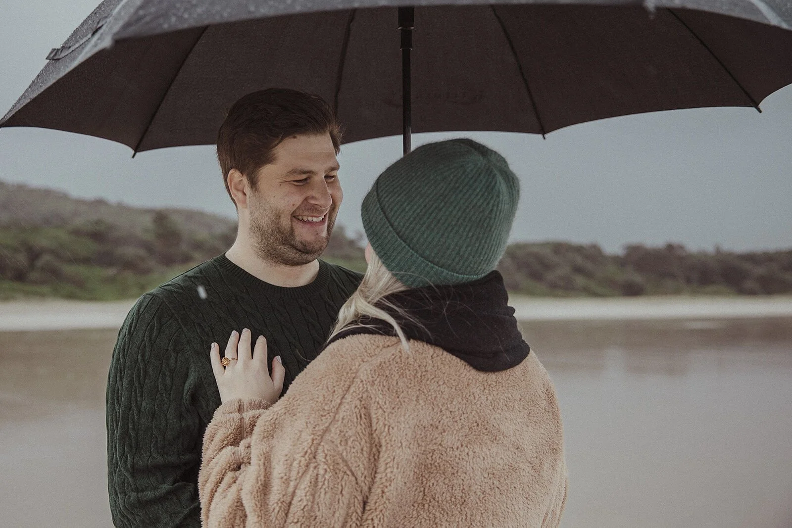 Newly engaged couple laughing together under an umbrella at Broken Head, proposal photographer Byron Bay
