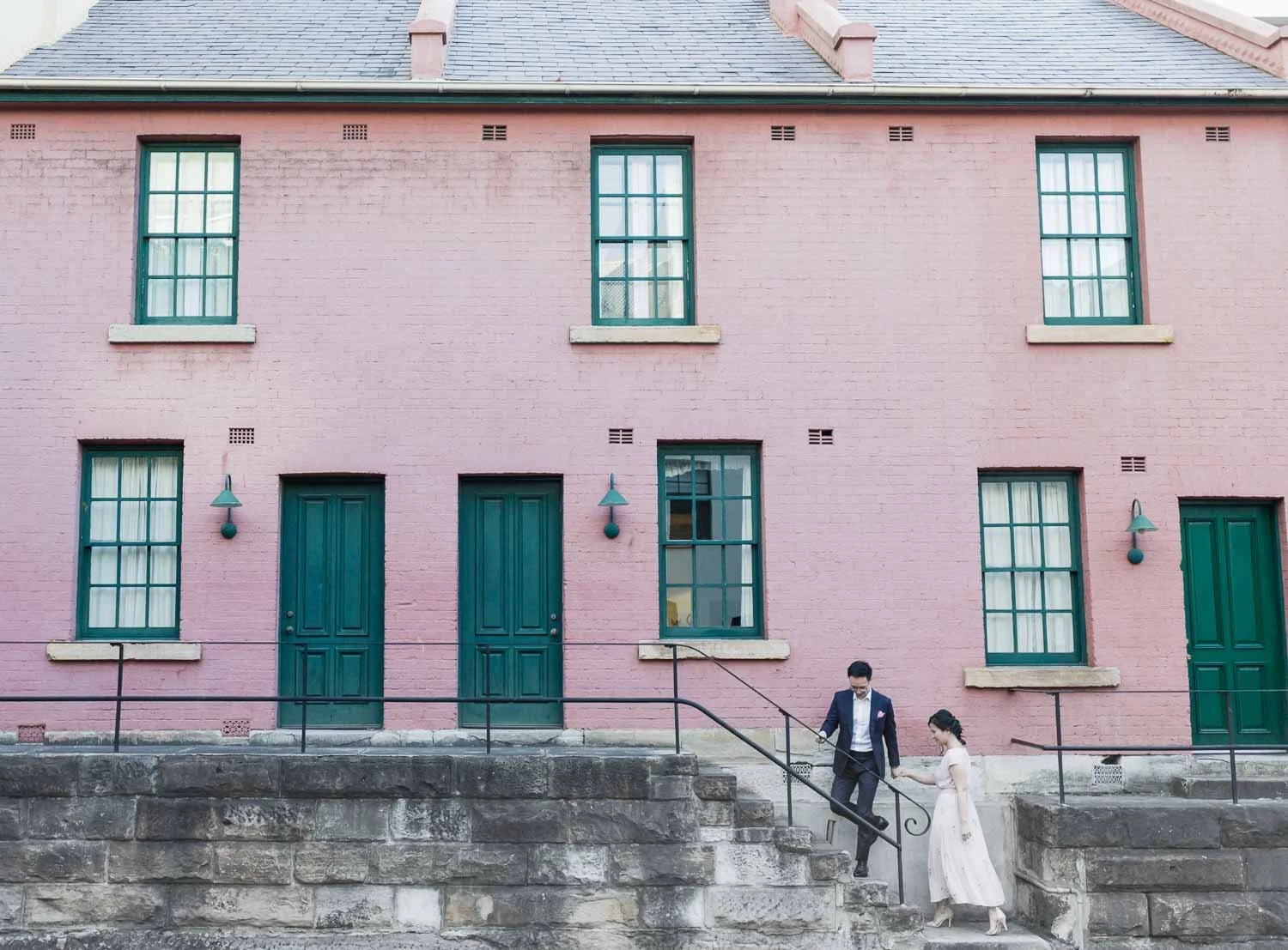 Couple walking down sandstone steps past pink terrace houses in The Rocks