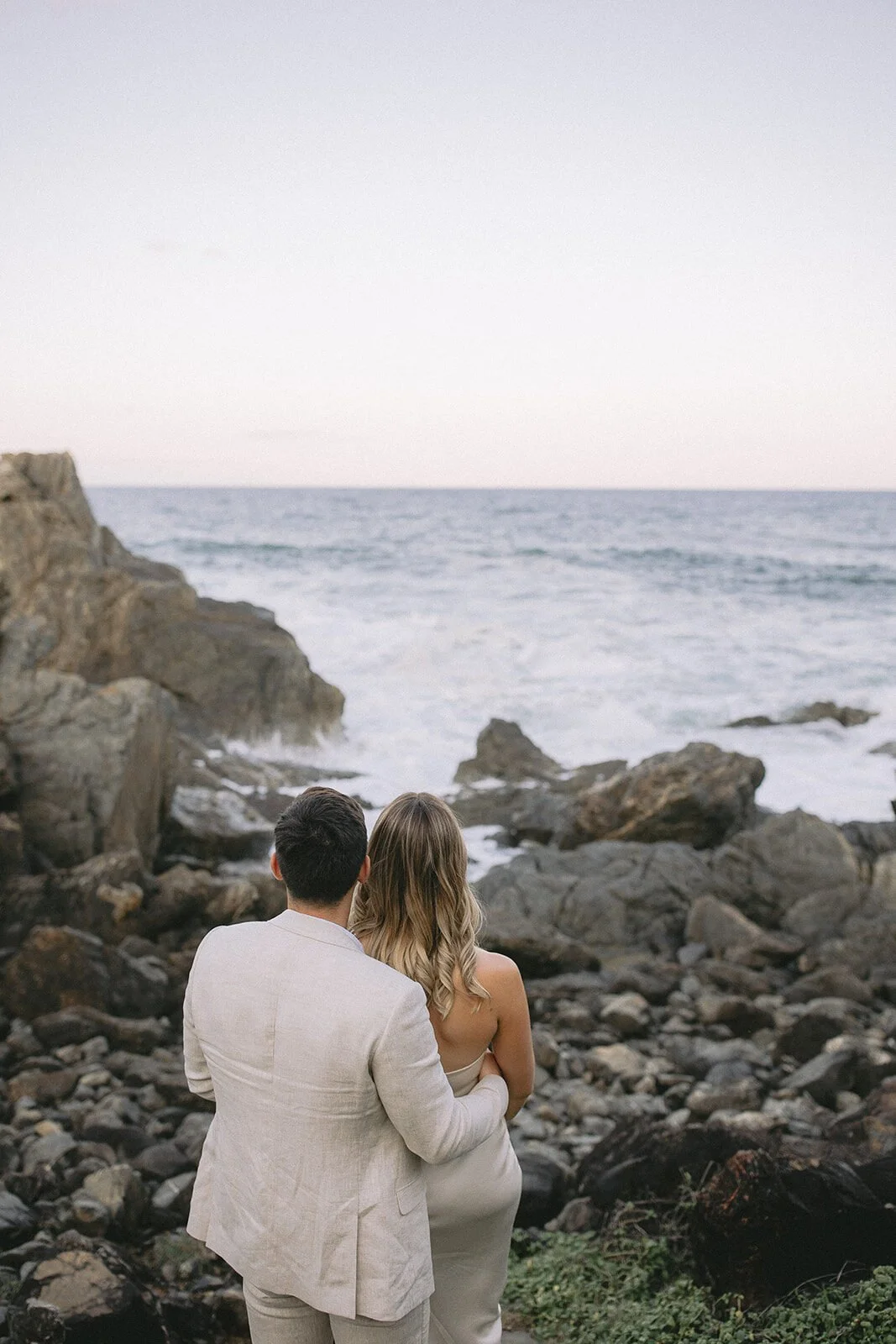 Couple embracing and looking out over the ocean from the rocks, Abby and James' elopement at Little Wategos Beach, Byron Bay