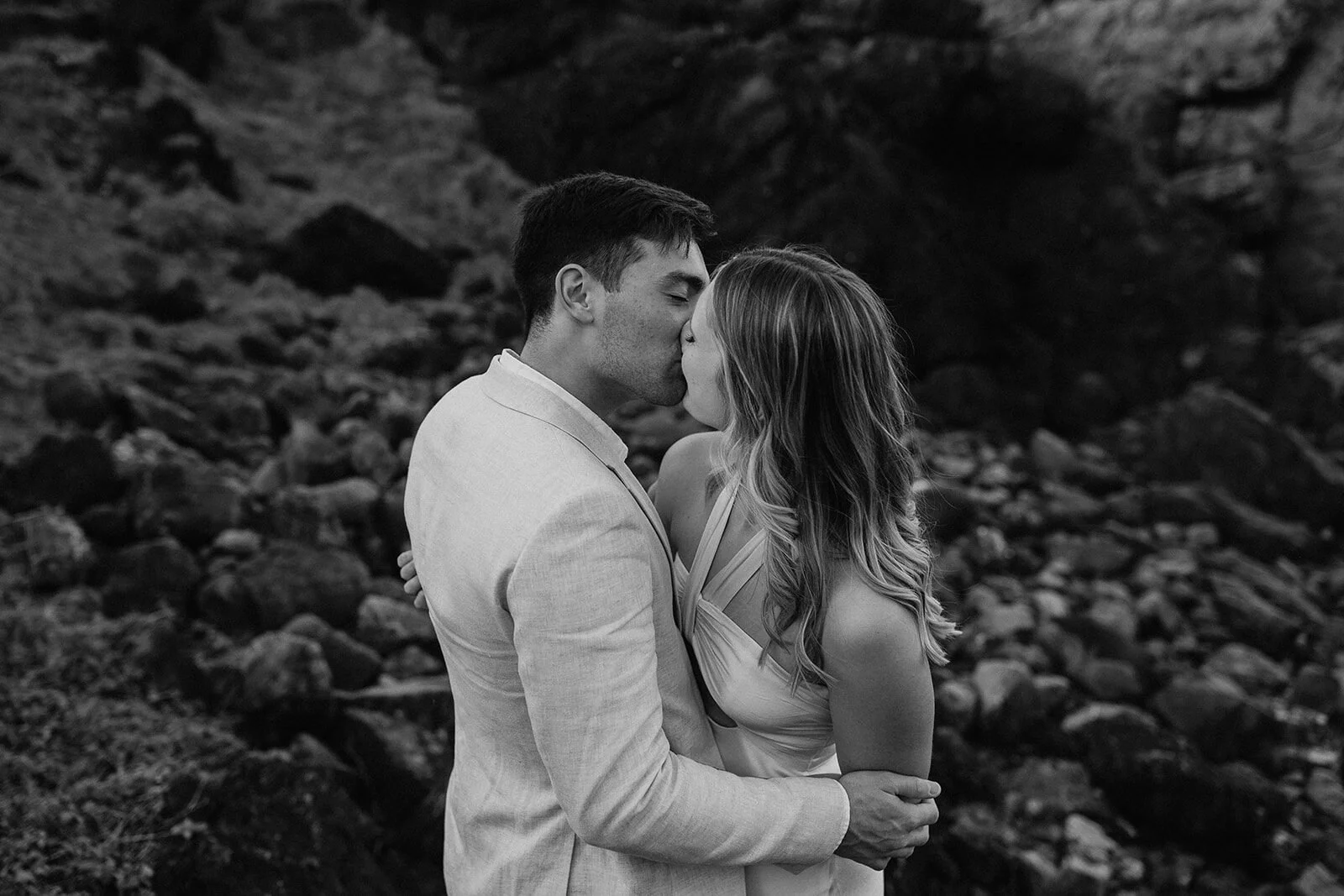 Black and white of the groom kissing the bride on the rocks, Abby and James' elopement at Little Wategos Beach, Byron Bay