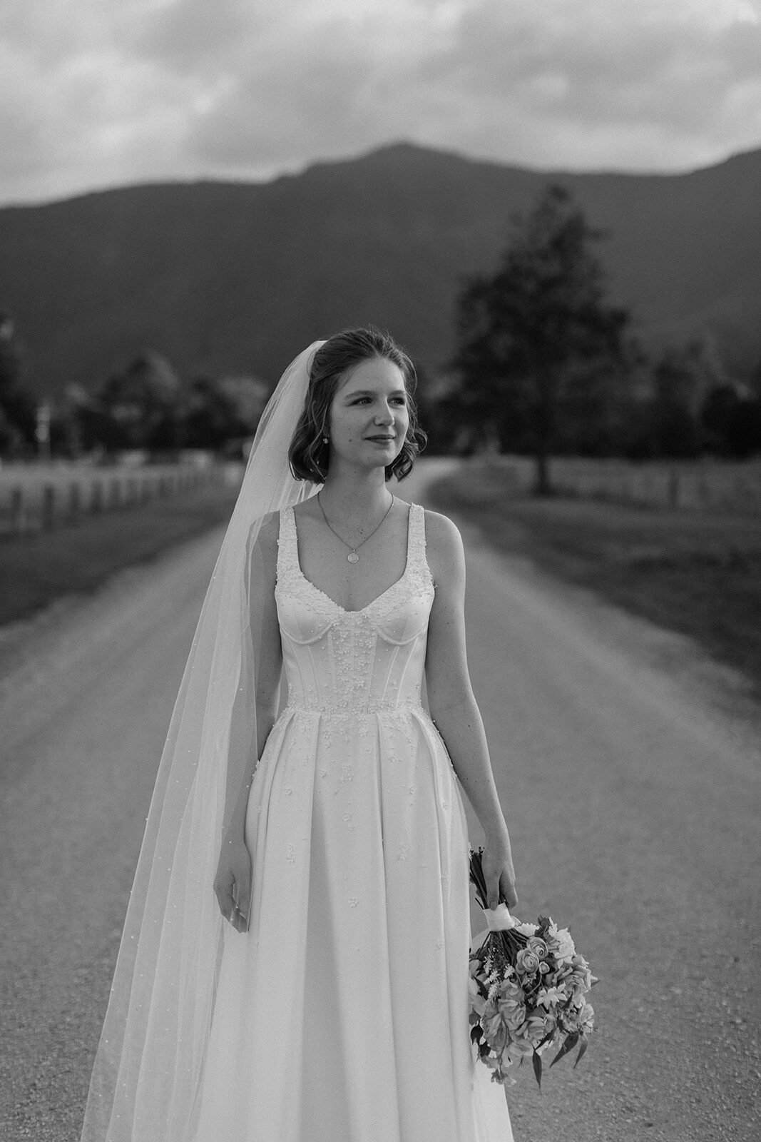 Black and white of the bride with her bouquet on the road, Sam and Tom's elopement at Highfield Farm, Northern Rivers
