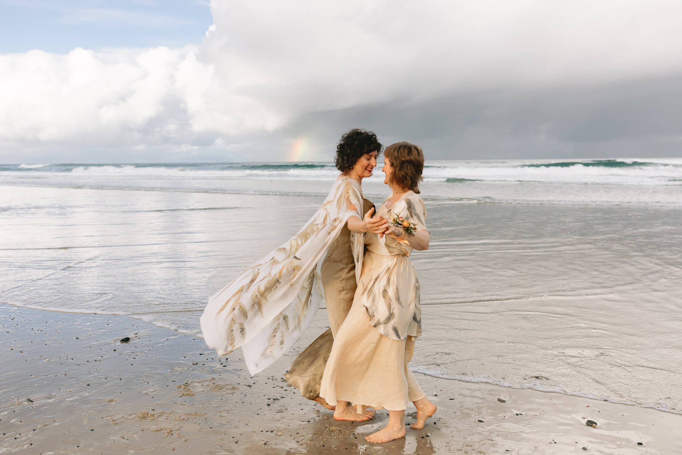 Two brides embracing at the water’s edge on Seven Mile Beach, Lennox Head