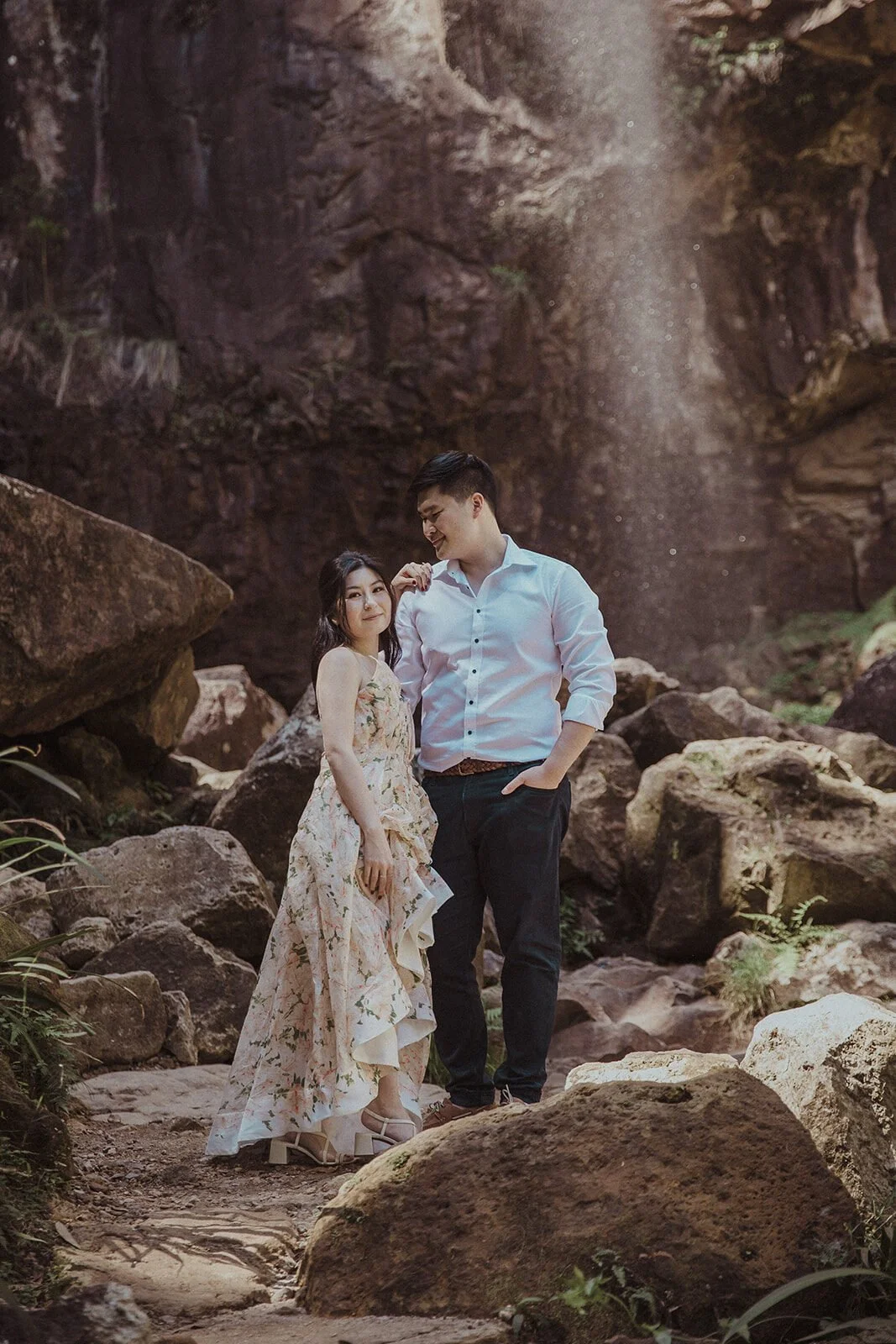 Couple posing on boulders in front of the waterfall, Maggie and William's pre-wedding photos in Byron Bay