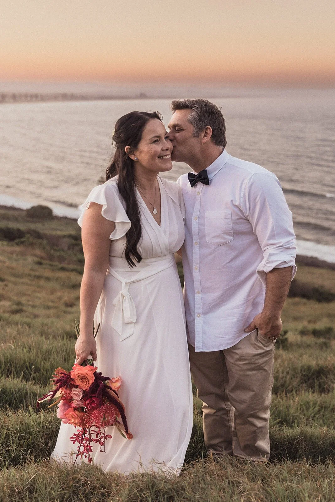 Groom kissing the bride's cheek on the headland, Maritess and Mark's elopement at Lennox Head