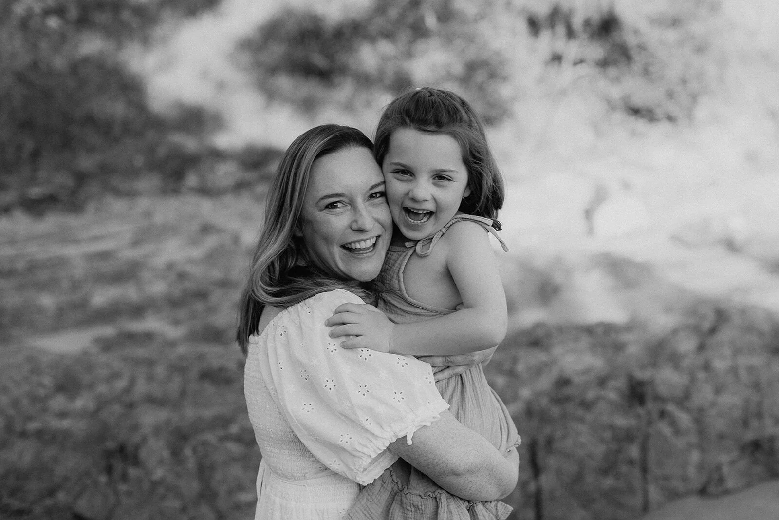 Black and white portrait of a mum and daughter laughing and hugging among the rocks