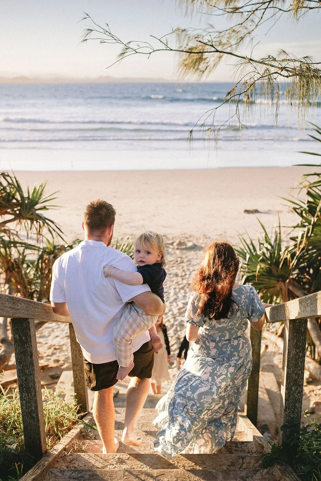 Dad carrying his toddler and mum walking down the beach steps toward the sand