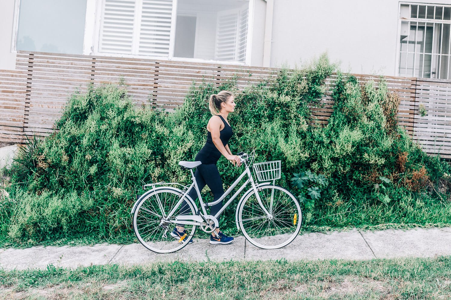 Woman with a vintage bicycle in front of a green hedge in Bondi