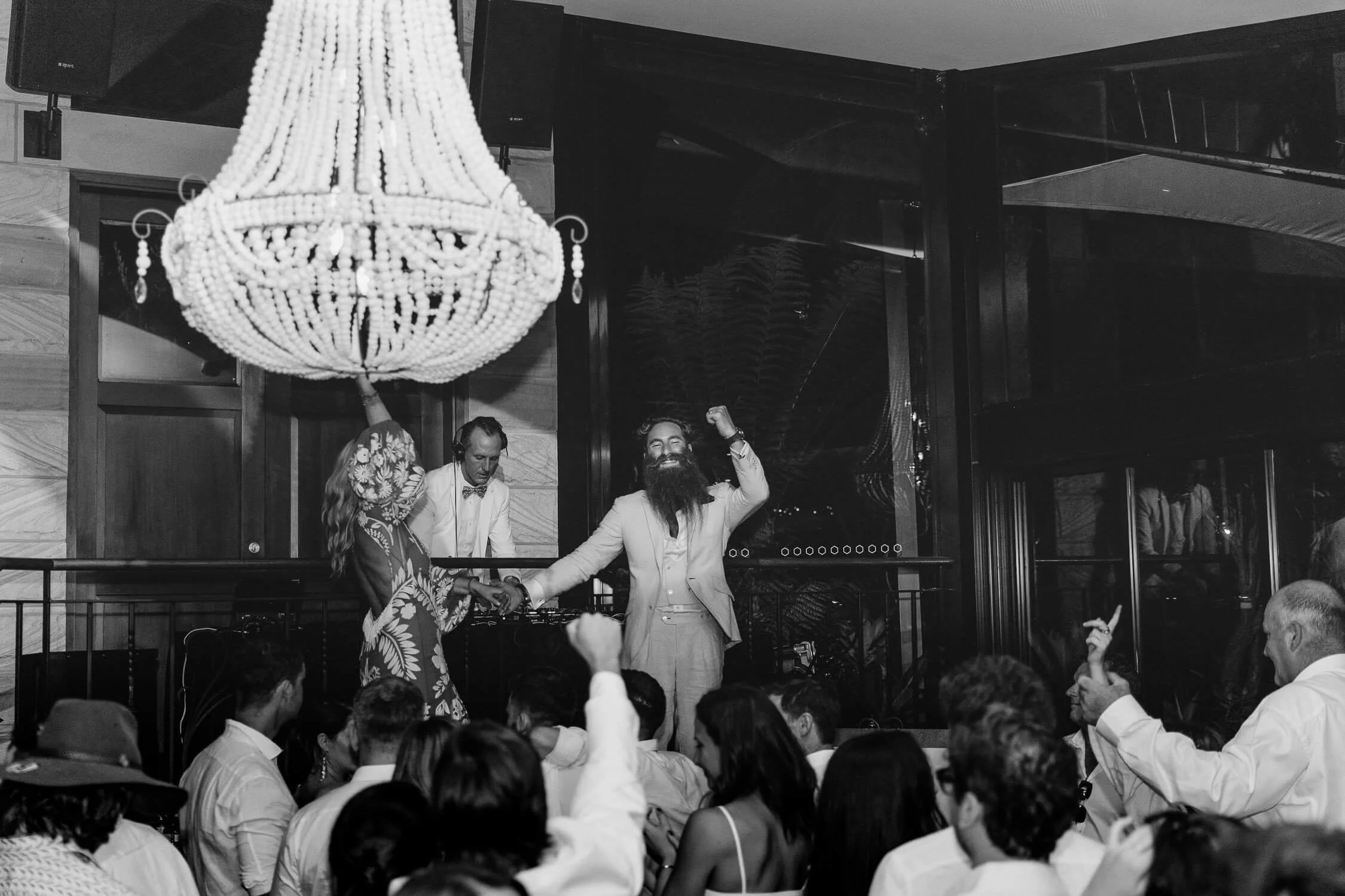 Black and white of guests dancing under a chandelier at a Tumbling Waters wedding, Stanwell Tops