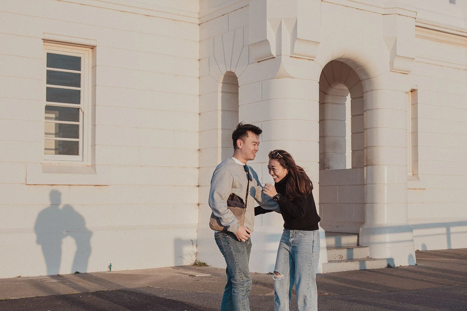 Couple laughing together after the proposal beside the lighthouse arches, Douglas and Ying's sunset marriage proposal at Cape Byron Lighthouse, Byron Bay