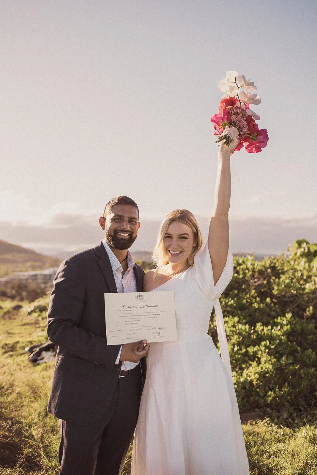 Bride raising her bouquet while the groom holds their marriage certificate, Brittany and Mark's elopement at Cabarita Beach, Northern Rivers