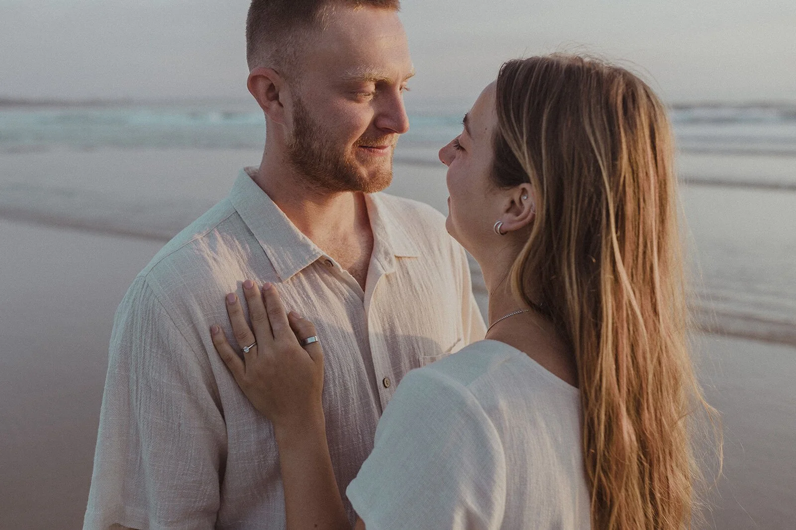 Close up of the couple smiling with her ringed hand on his shirt, Charlie and Hannah's sunrise marriage proposal at Broken Head Beach, Byron Bay