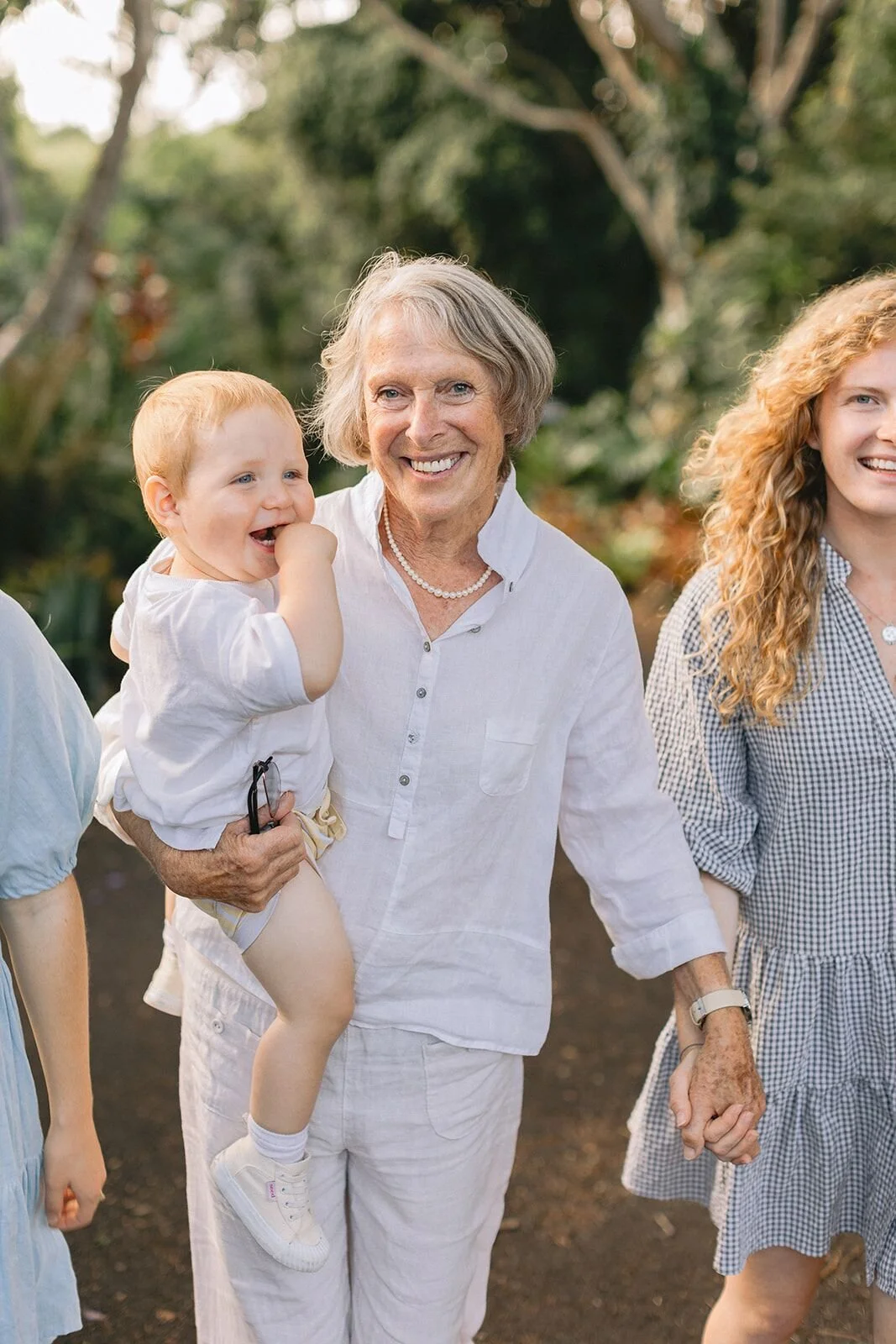 Smiling grandmother carrying her laughing baby grandson on a garden path