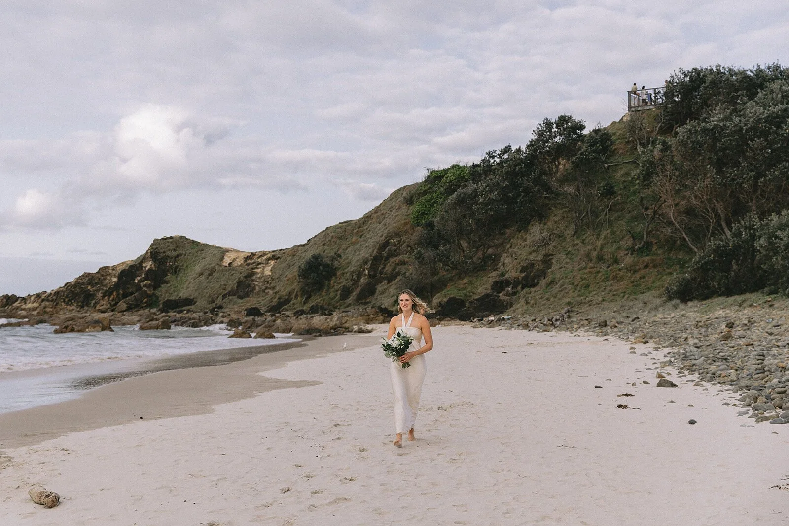 Bride walking along the sand toward the headland, Abby and James' elopement at Little Wategos Beach, Byron Bay