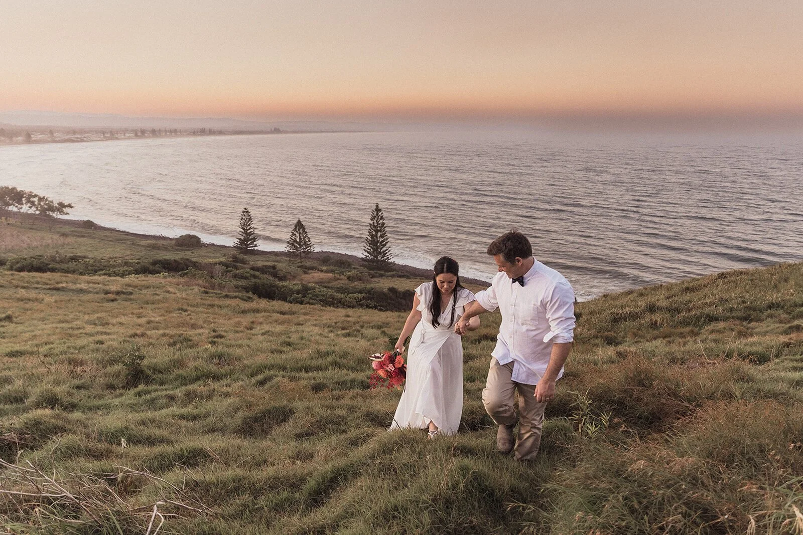 Couple walking down the grassy headland at sunset, Maritess and Mark's elopement at Lennox Head