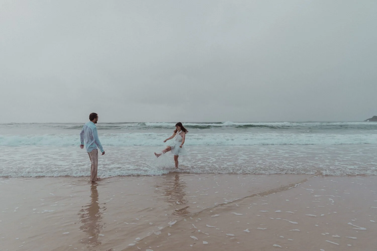 Couple splashing in the waves, Yoanne and Elisa's rainy elopement at Broken Head, Byron Bay