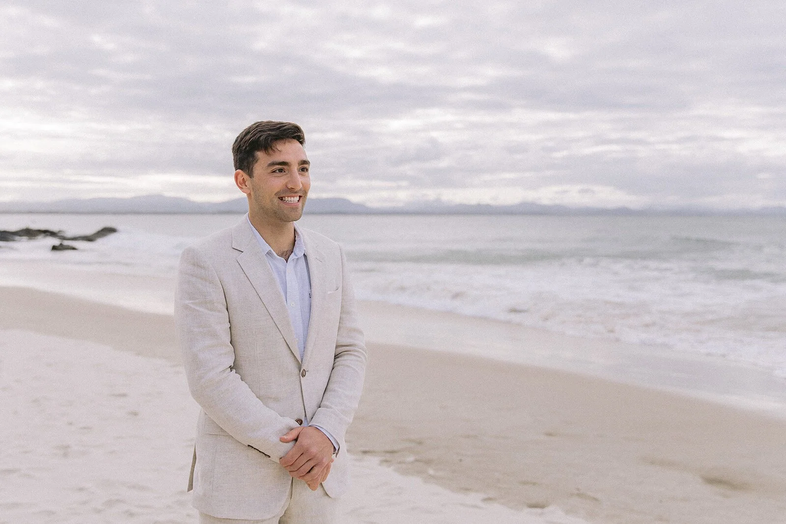 Groom in a linen suit smiling on the beach, Abby and James' elopement at Little Wategos Beach, Byron Bay