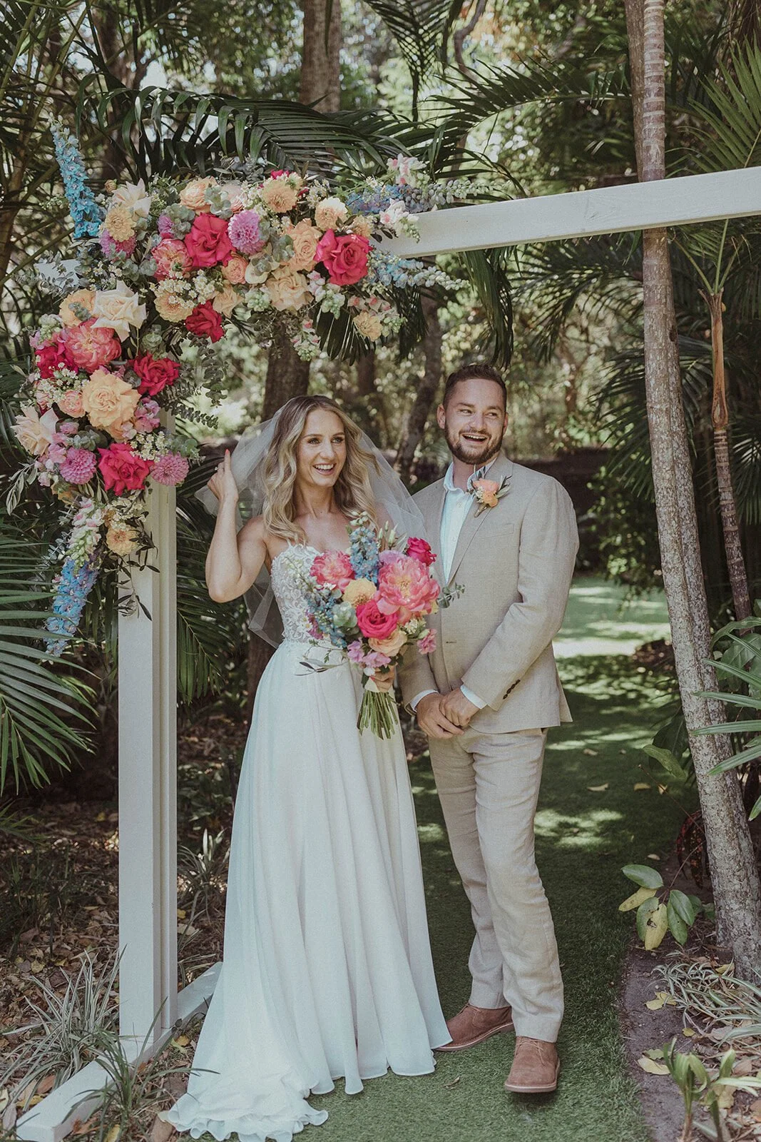 Couple beneath a floral arch in a tropical garden, Eliza and Greg's elopement at Broken Head, Byron Bay