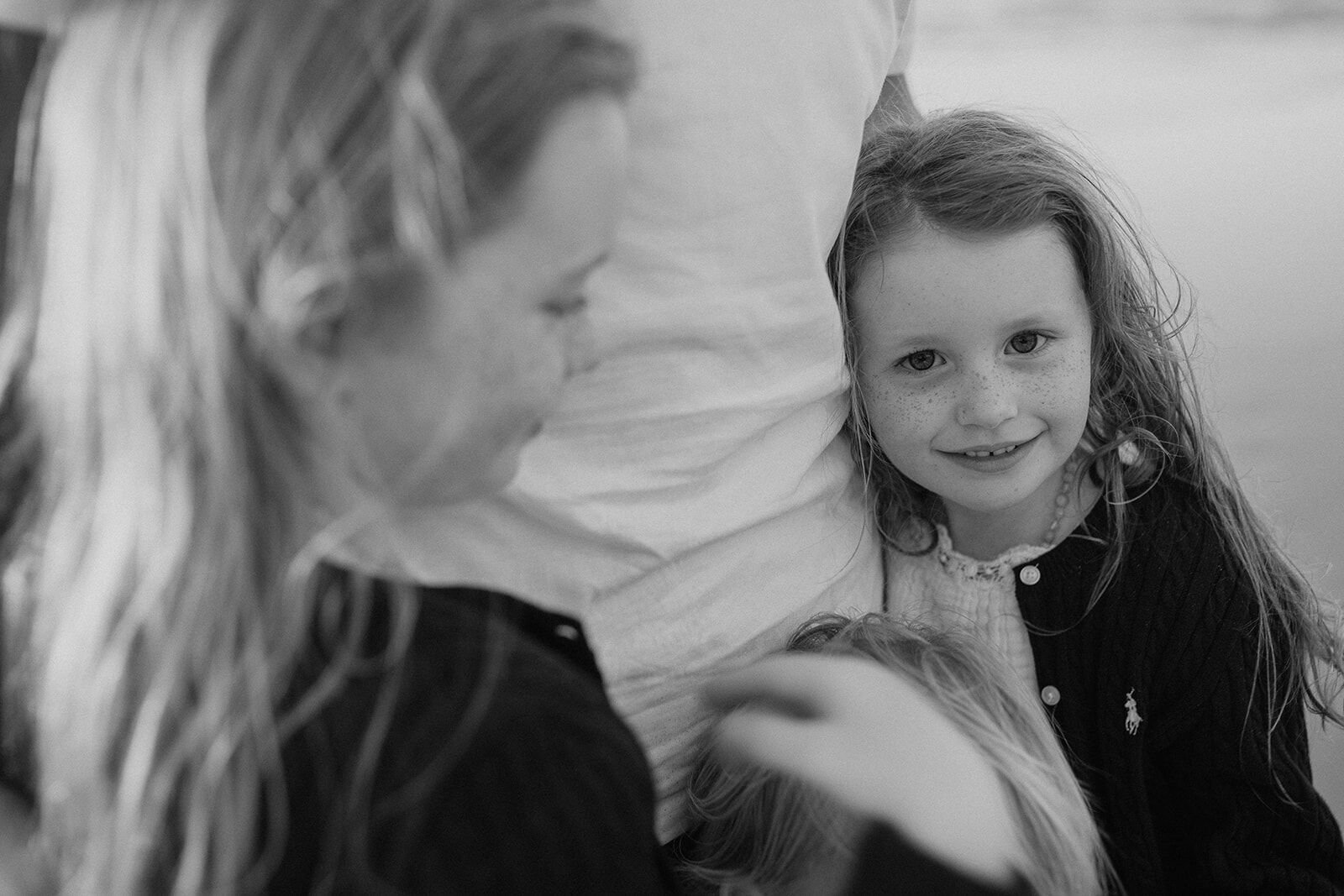 Black and white close-up of a young girl smiling at the camera, leaning against her parent