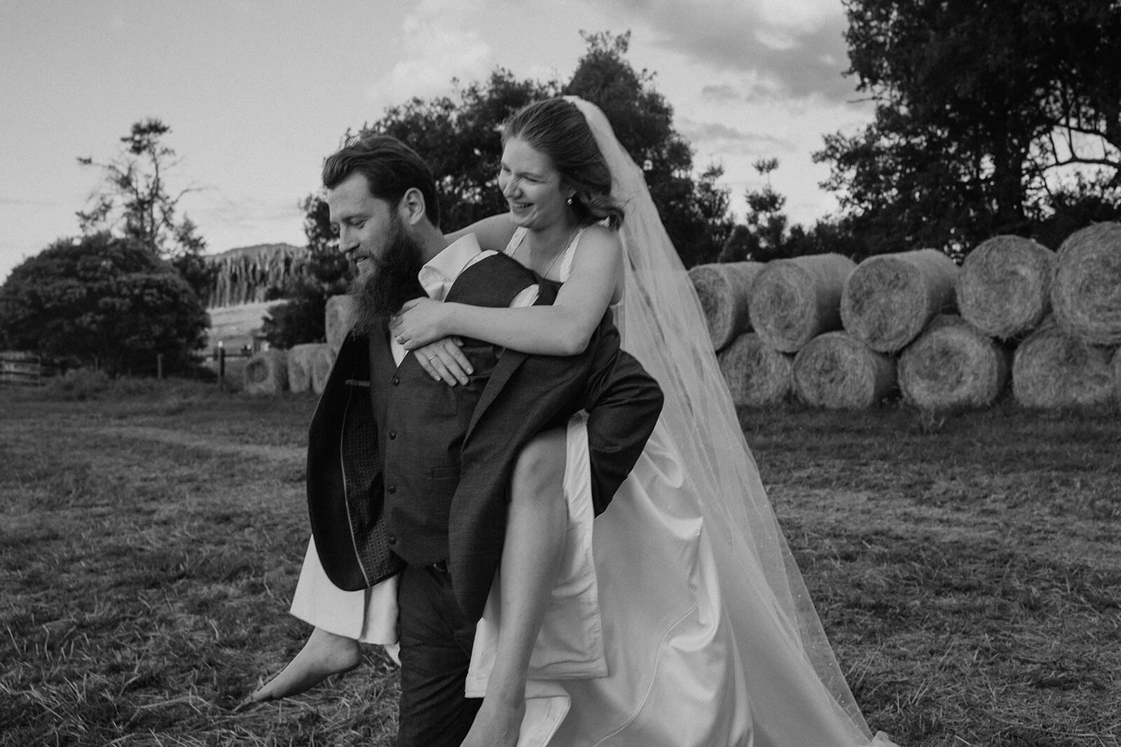 Black and white of the groom giving the bride a piggyback, Sam and Tom's elopement at Highfield Farm, Northern Rivers