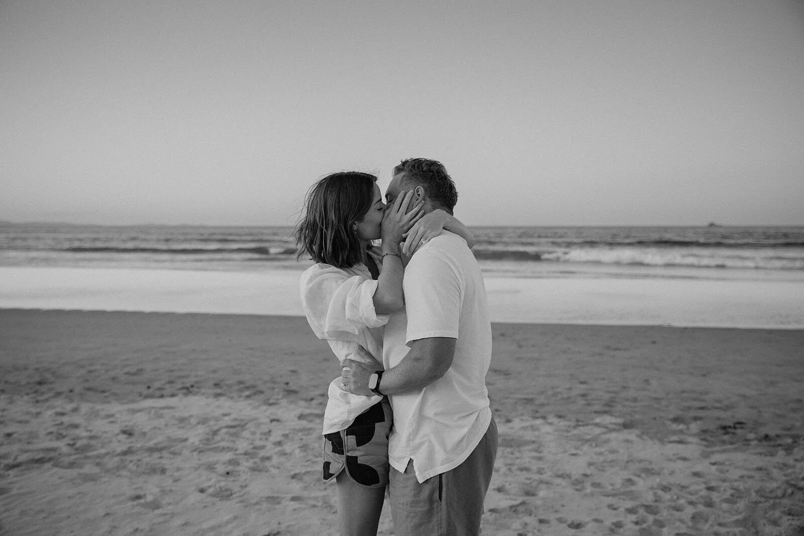 Black and white of the couple kissing on the beach, Jamie and Jessica's beach marriage proposal at Belongil Beach, Byron Bay