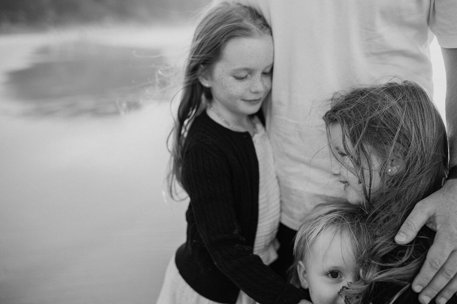 Black and white close-up of two sisters and their toddler brother leaning in against their dad