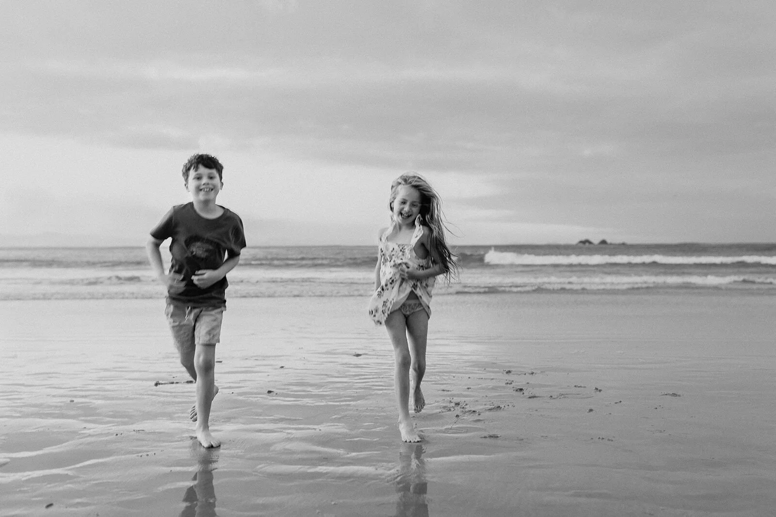 Black and white photo of a brother and sister running along the shoreline together