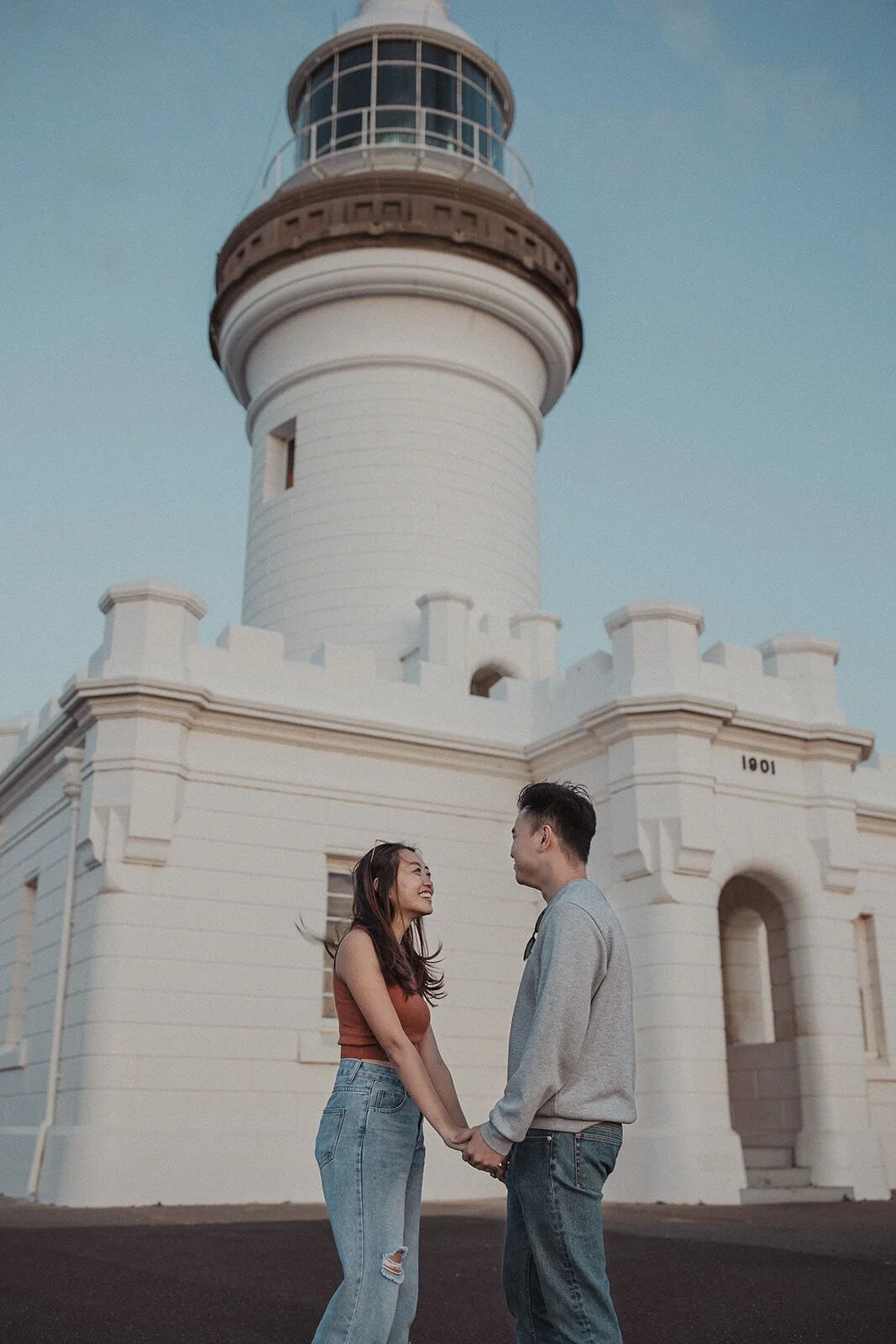 Couple holding hands in front of the Cape Byron Lighthouse tower, Douglas and Ying's sunset marriage proposal at Cape Byron Lighthouse, Byron Bay