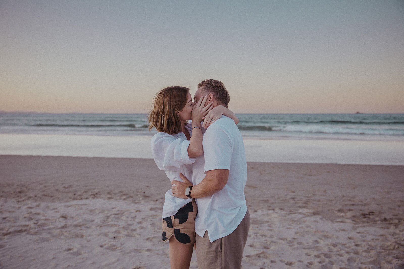 Couple kissing at the water's edge at dusk, Jamie and Jessica's beach marriage proposal at Belongil Beach, Byron Bay