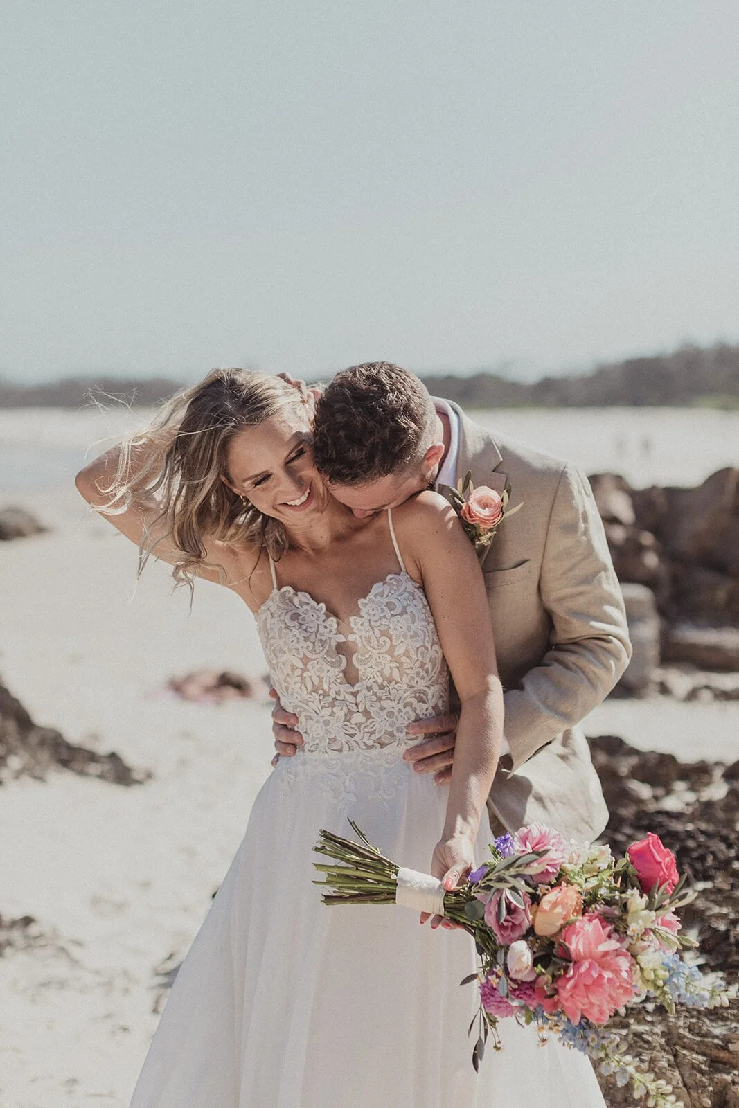 Groom kissing the bride's shoulder on the beach, Eliza and Greg's elopement at Broken Head, Byron Bay