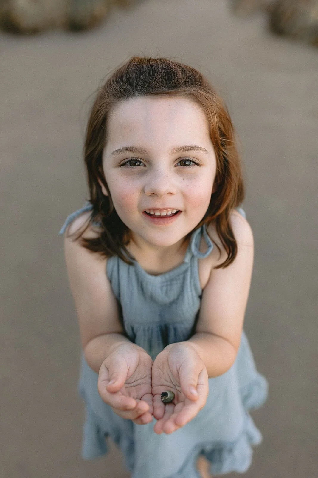 Girl smiling up at the camera while holding a small hermit crab in her cupped hands