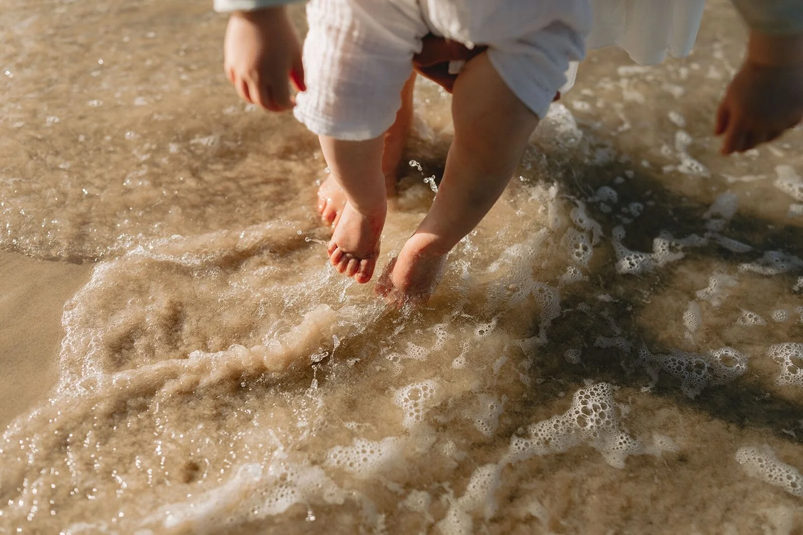 Toddler's bare feet in the swirling shallow water at the edge of the shore