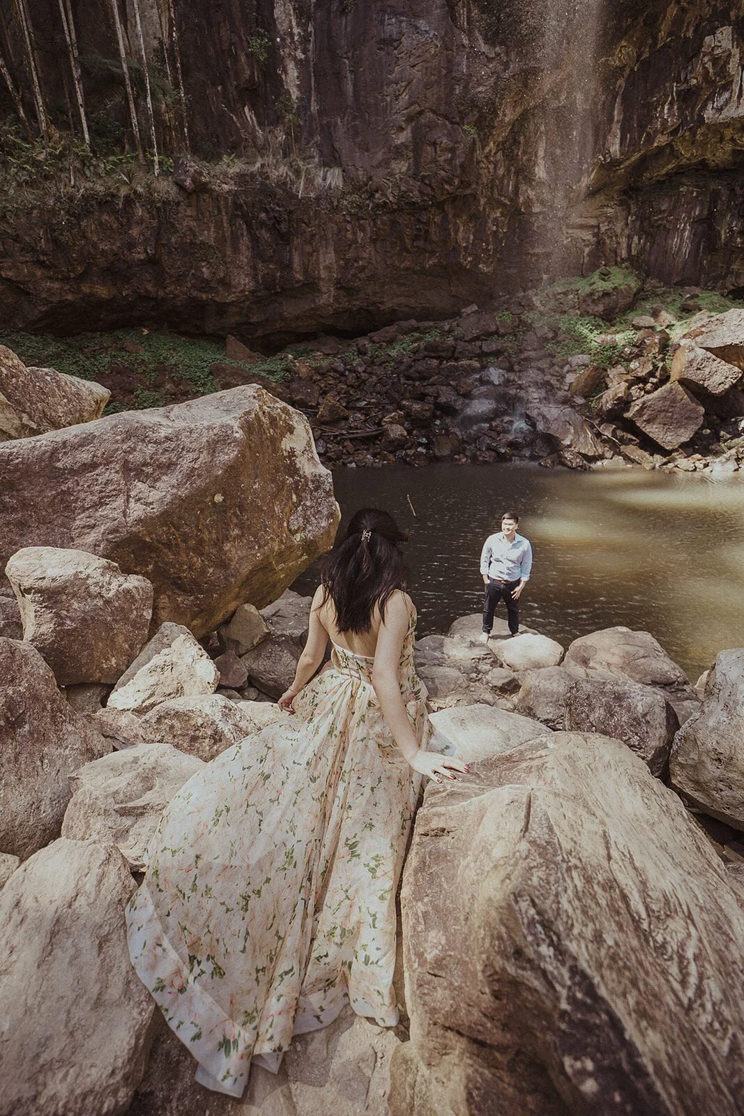 Couple at a waterfall pool with the bride in a flowing floral dress on the boulders, Maggie and William's pre-wedding photos in Byron Bay