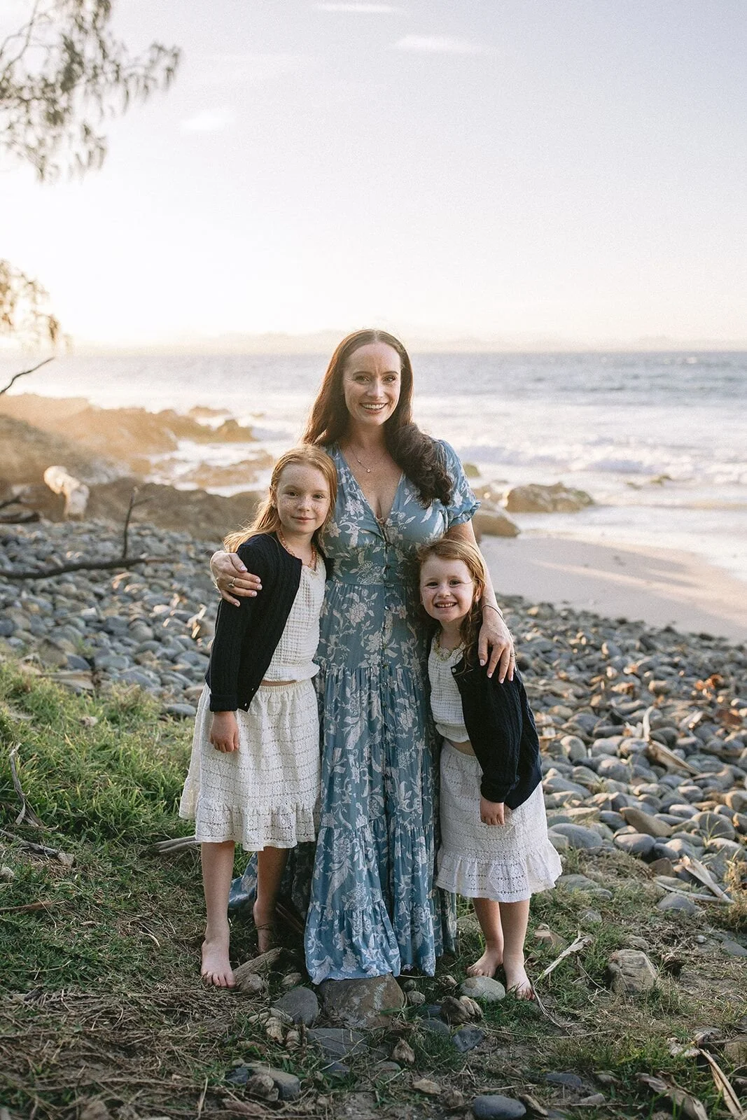 Mum with her two daughters on the rocky shore at Wategos Beach, Byron Bay, in soft evening light