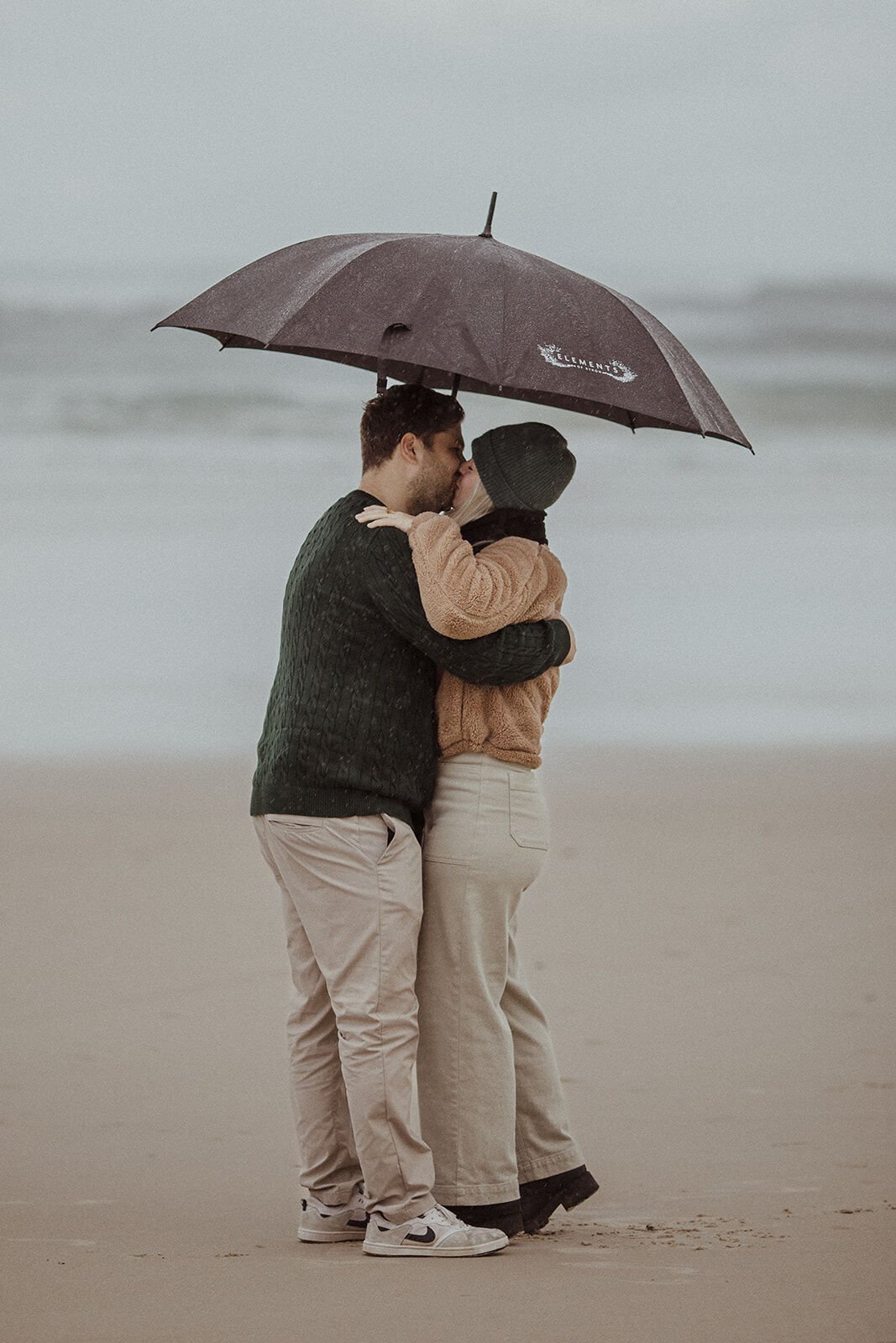 Couple hugging under the umbrella after the proposal on a rainy beach, Raphael and Vany's rainy day marriage proposal at Broken Head Beach, Byron Bay