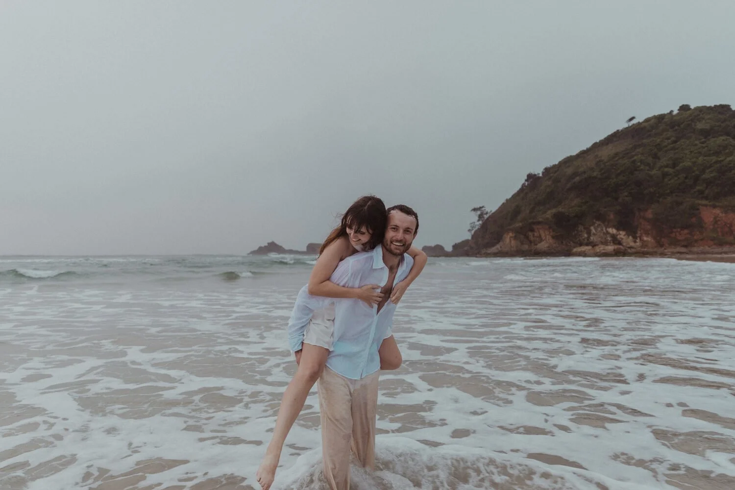 Bride on the groom's back in the surf, Yoanne and Elisa's rainy elopement at Broken Head, Byron Bay