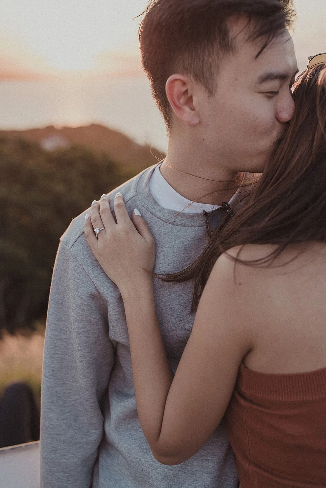 Close up of a kiss with the engagement ring on her hand resting on his shoulder, Douglas and Ying's sunset marriage proposal at Cape Byron Lighthouse, Byron Bay