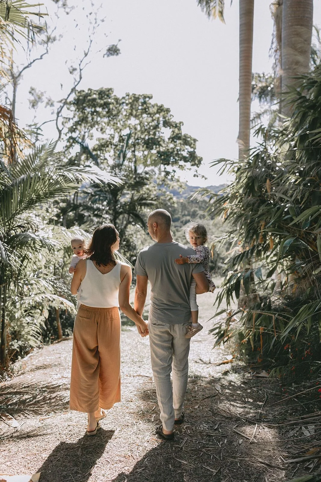 Mum and dad holding hands and carrying their two daughters along a garden path