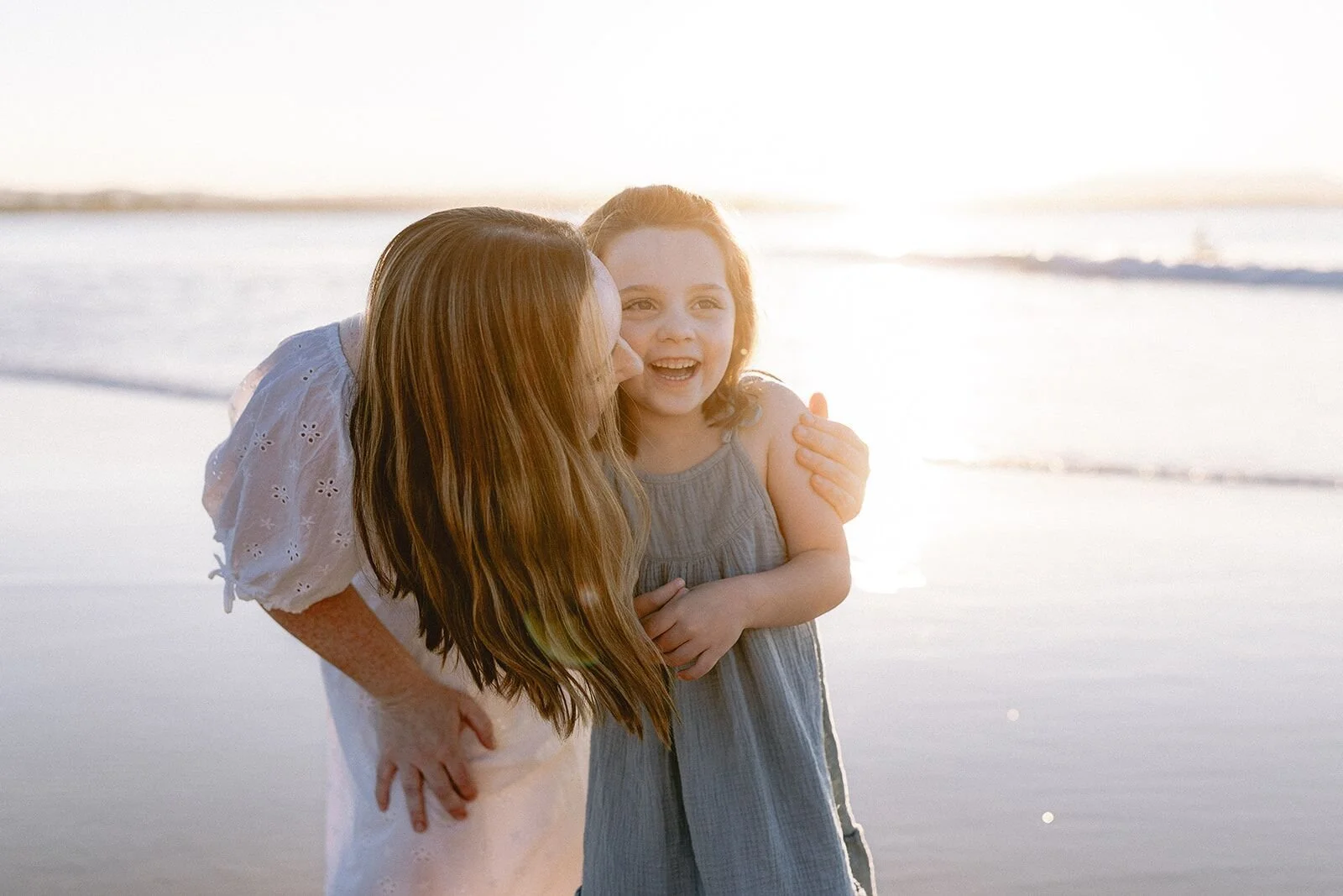 Mum hugging and kissing her daughter, both glowing in the setting sun