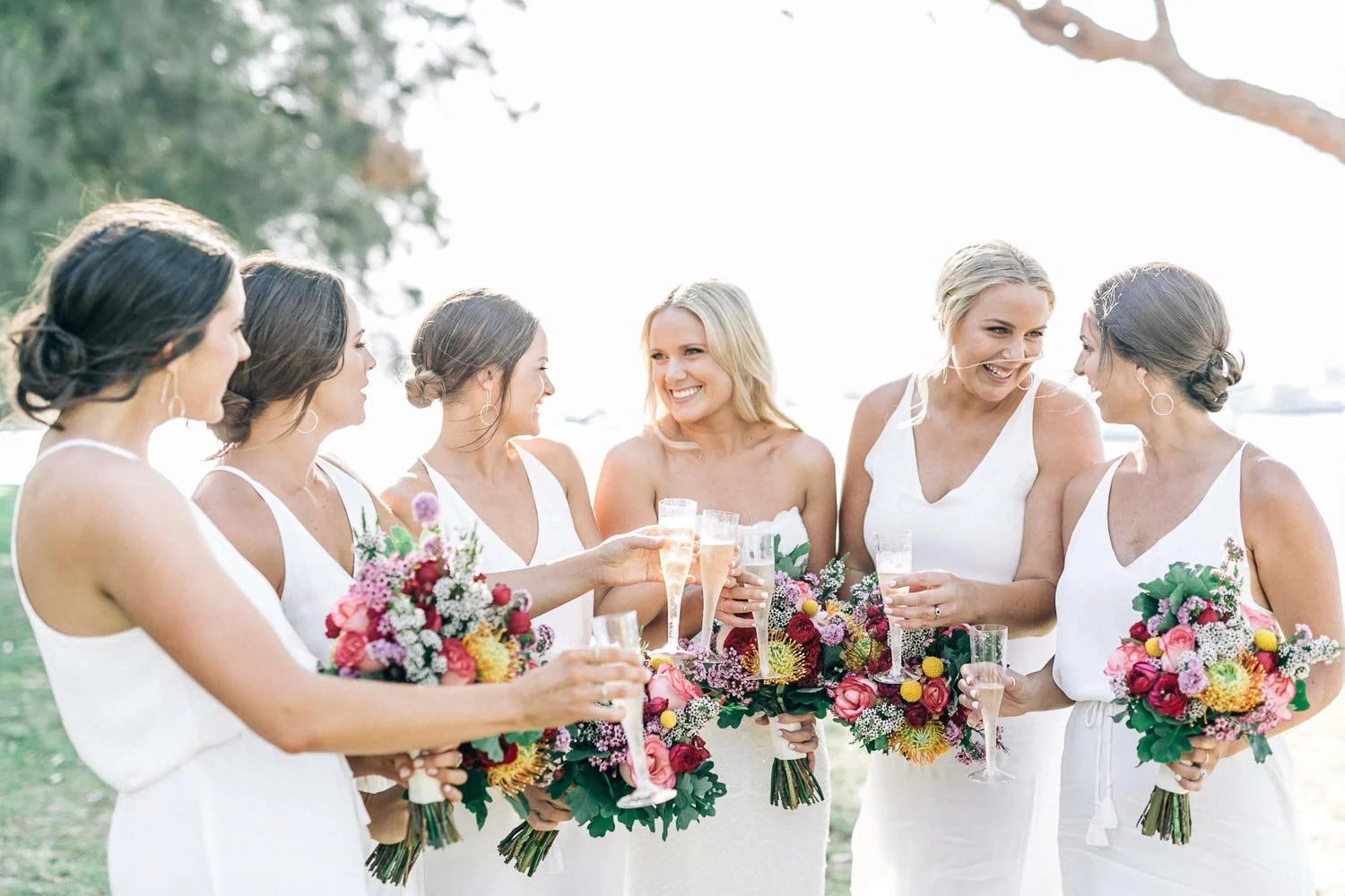 Bride laughing with her bridesmaids, bright bouquets in hand