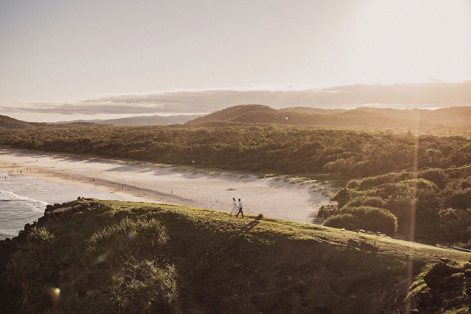 Tiny couple on the headland in golden light with the long beach beyond, Brittany and Mark's elopement at Cabarita Beach, Northern Rivers