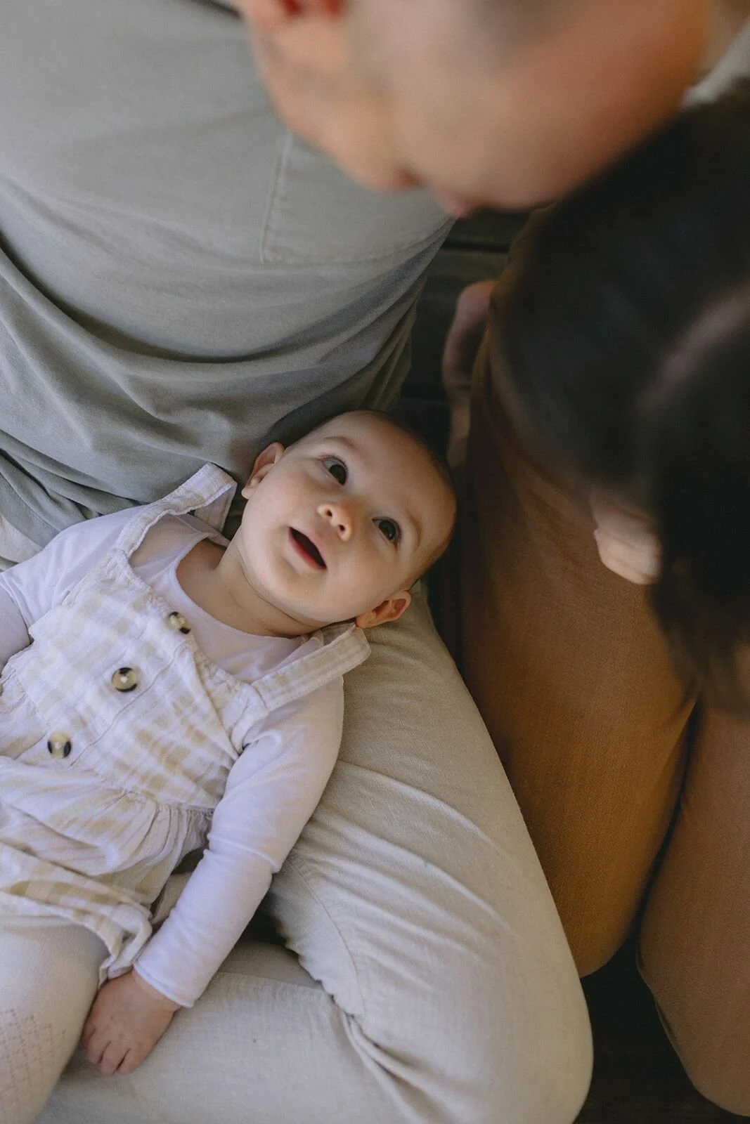 Baby lying in her parents' laps with a wide, delighted smile as dad kisses her
