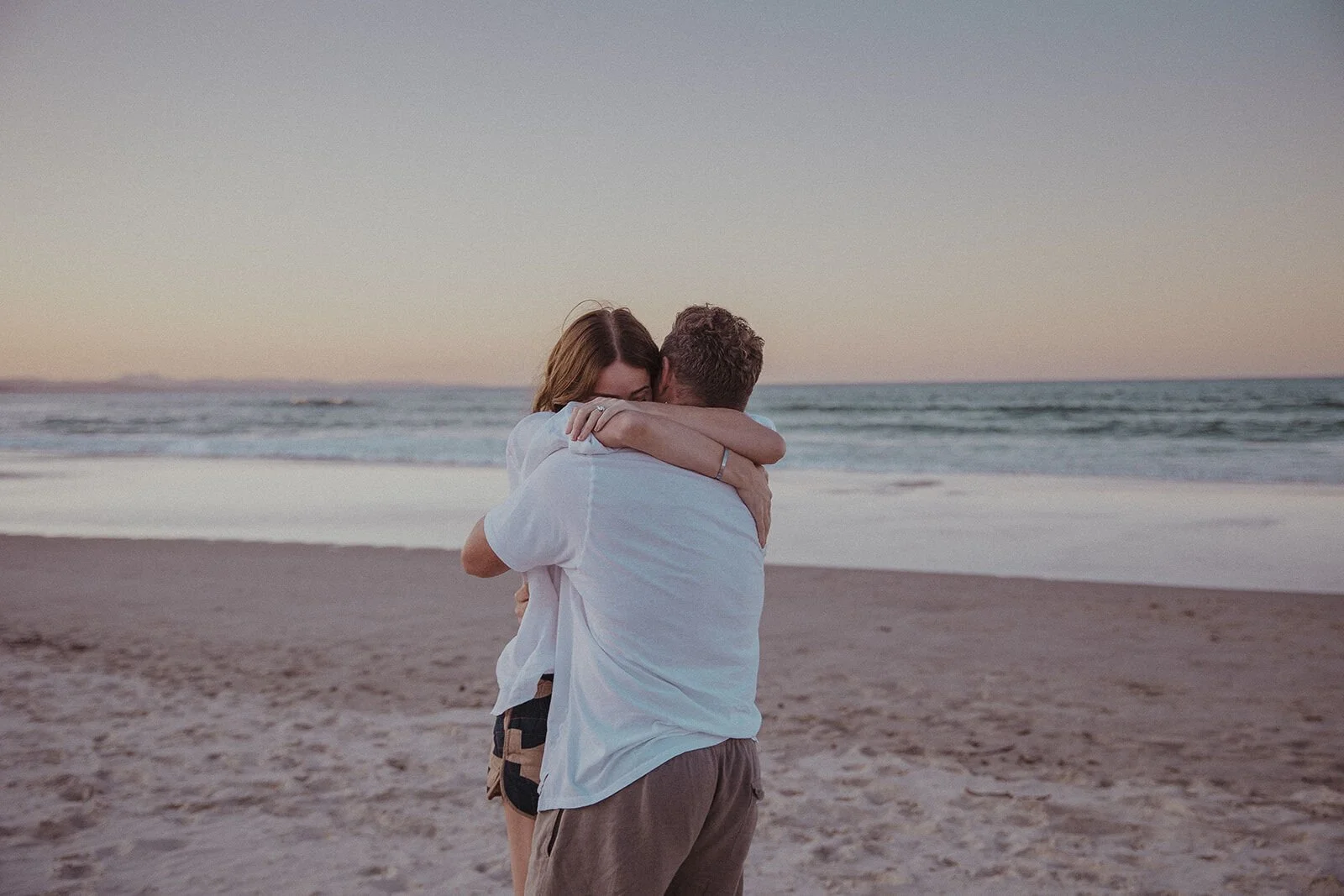 Couple embracing at dusk on the beach, Jamie and Jessica's beach marriage proposal at Belongil Beach, Byron Bay