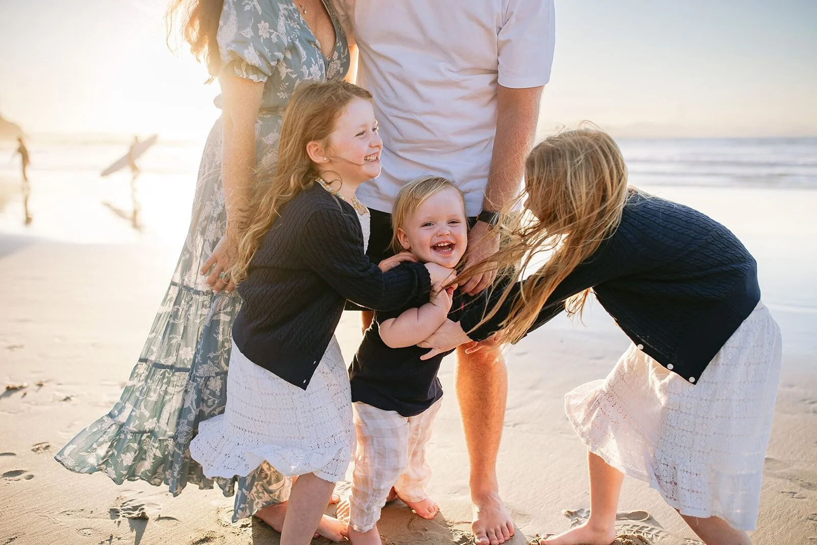 Two sisters and their little brother laughing and hugging in front of their parents on the beach
